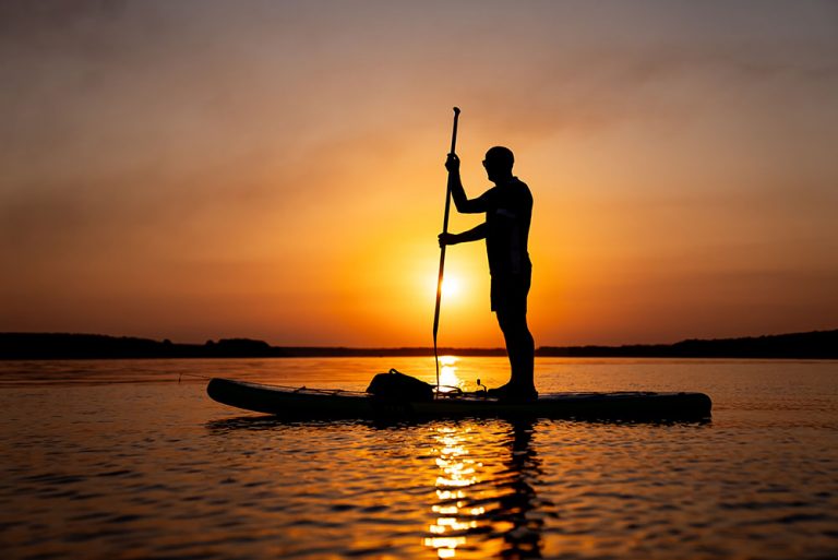 Silhouette einer Person beim Stand-Up-Paddling auf dem Uckersee während eines stimmungsvollen, orangeroten Sonnenuntergangs.